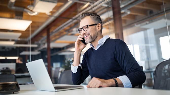 Man talking on phone while working on his laptop.