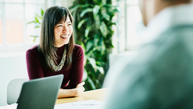 Woman smiling at board table with laptop beside her.