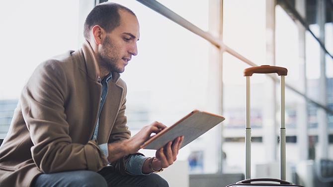 Male professional sitting in the airport using an iPad, reflecting the importance of duty of care in corporate travel management